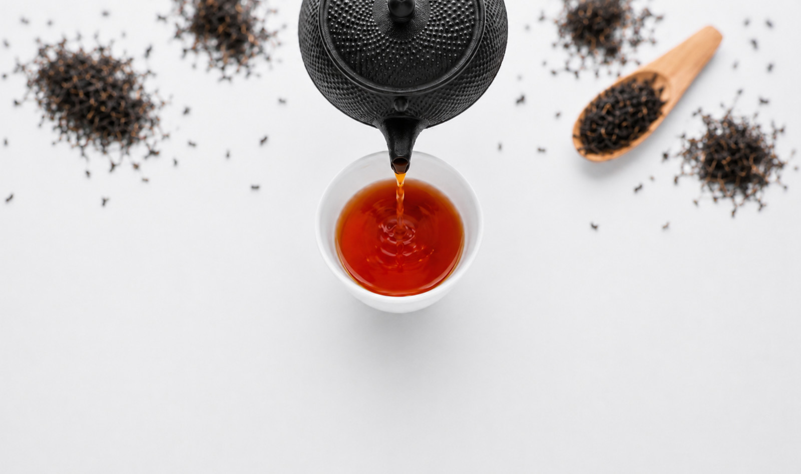 Tea being poured into a cup surrounded by loose Ceylon tea leaves